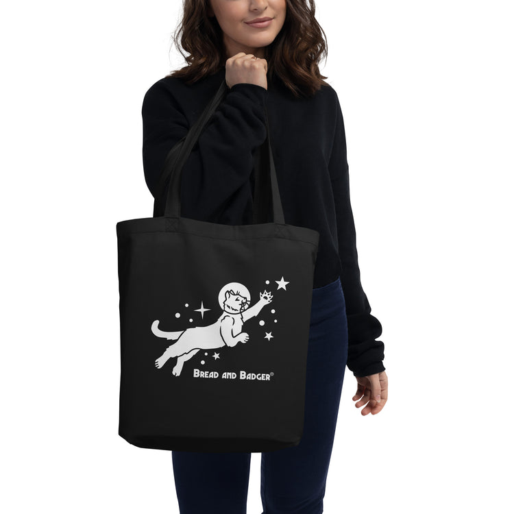 Woman holding a black tote bag with white astronaut cat graphic and 'Bread and Badger' text on a white background