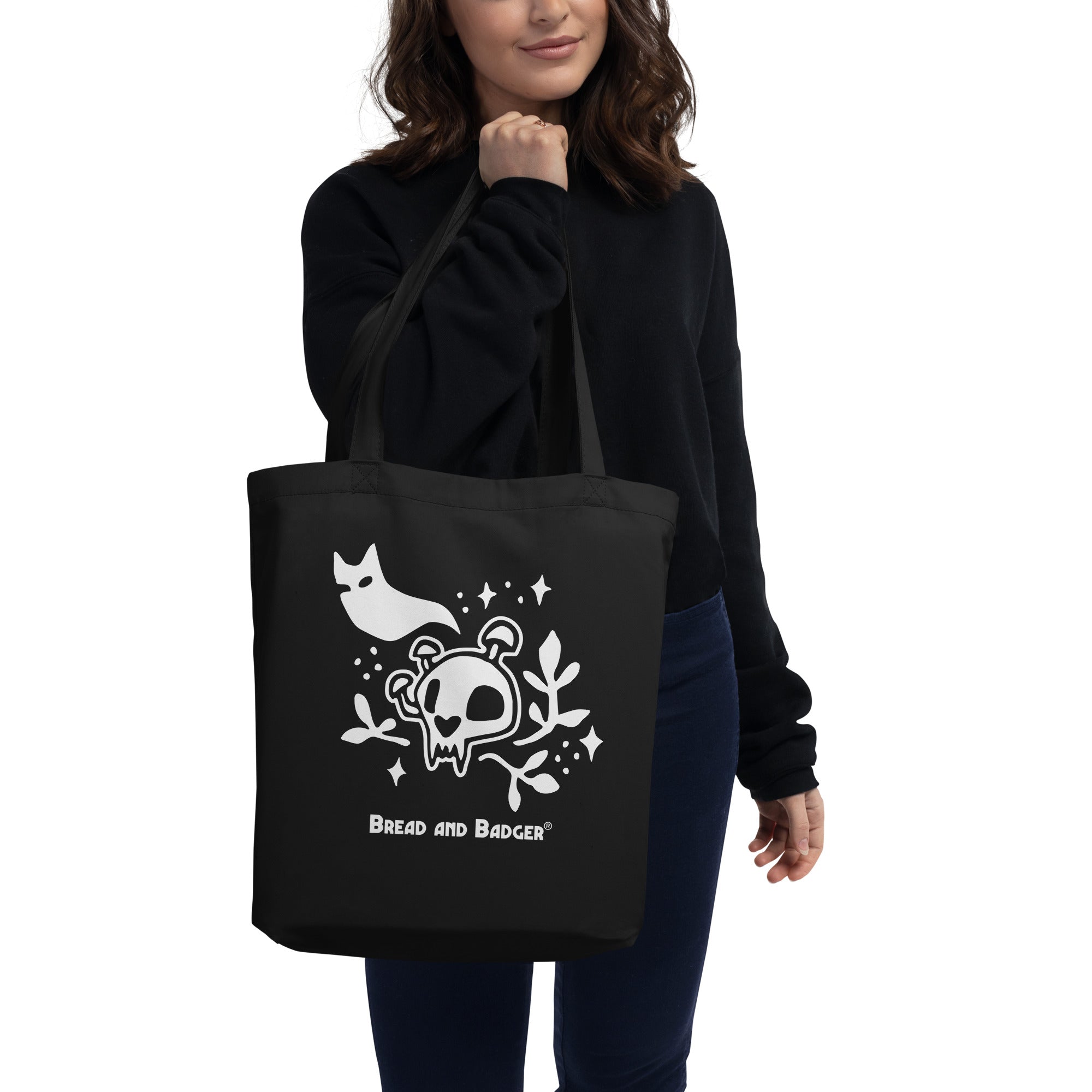 Person holding a black tote bag with white skull and cat ghost design and 'Bread and Badger' logo.