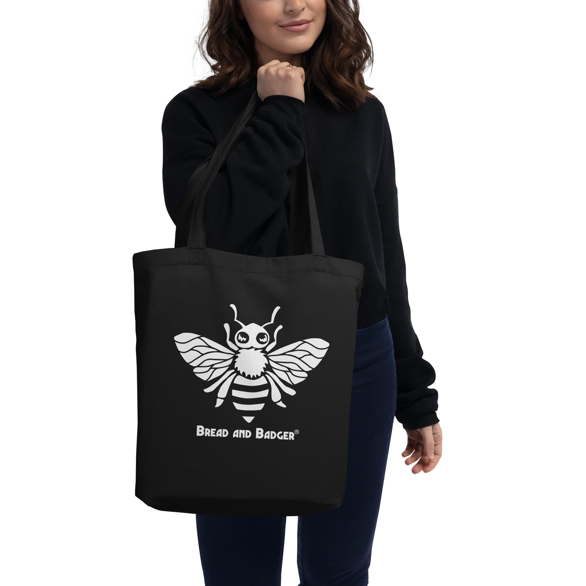 Person holding a black tote bag with a white bee design and 'Bread and Badger' text.