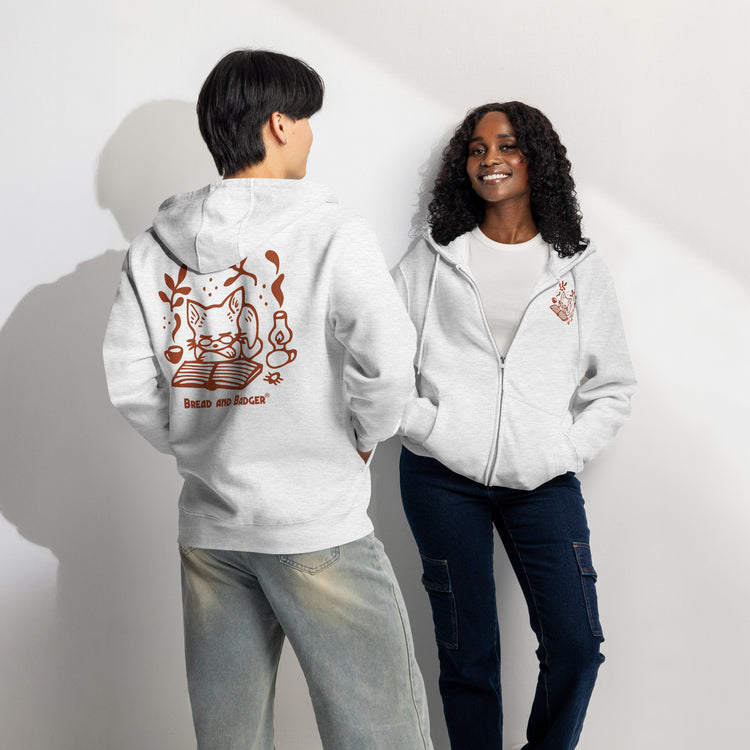 Two people wearing light heather grey hoodies with rust-red graphics on a plain background