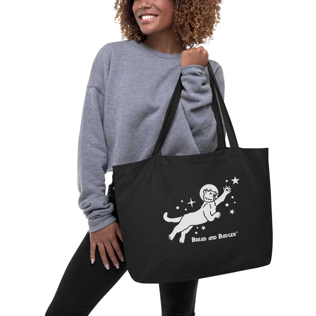 Woman holding a black tote bag with white astronaut cat graphic and 'Bread and Badger' text on a white background