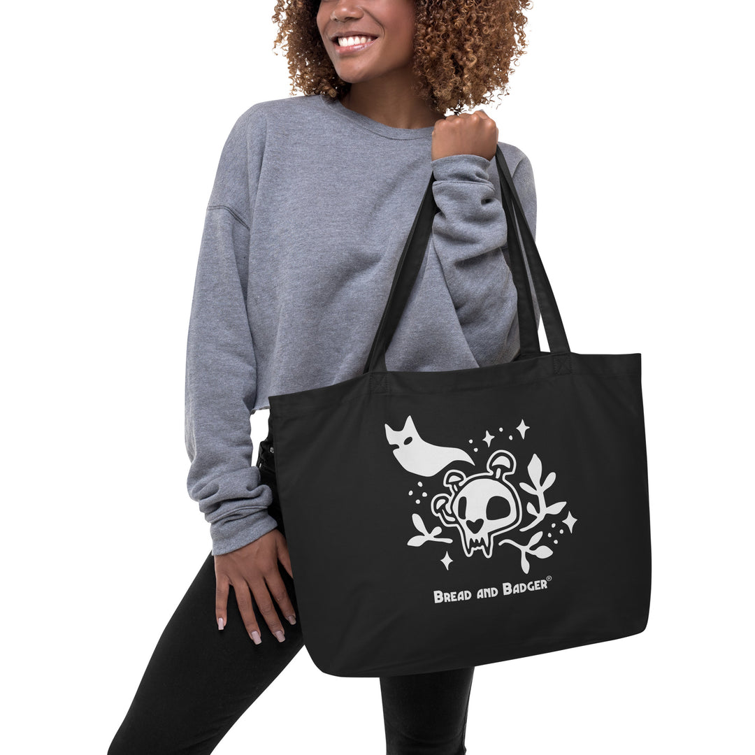 Person holding a black tote bag with white skull and cat ghost design and 'Bread and Badger' logo.