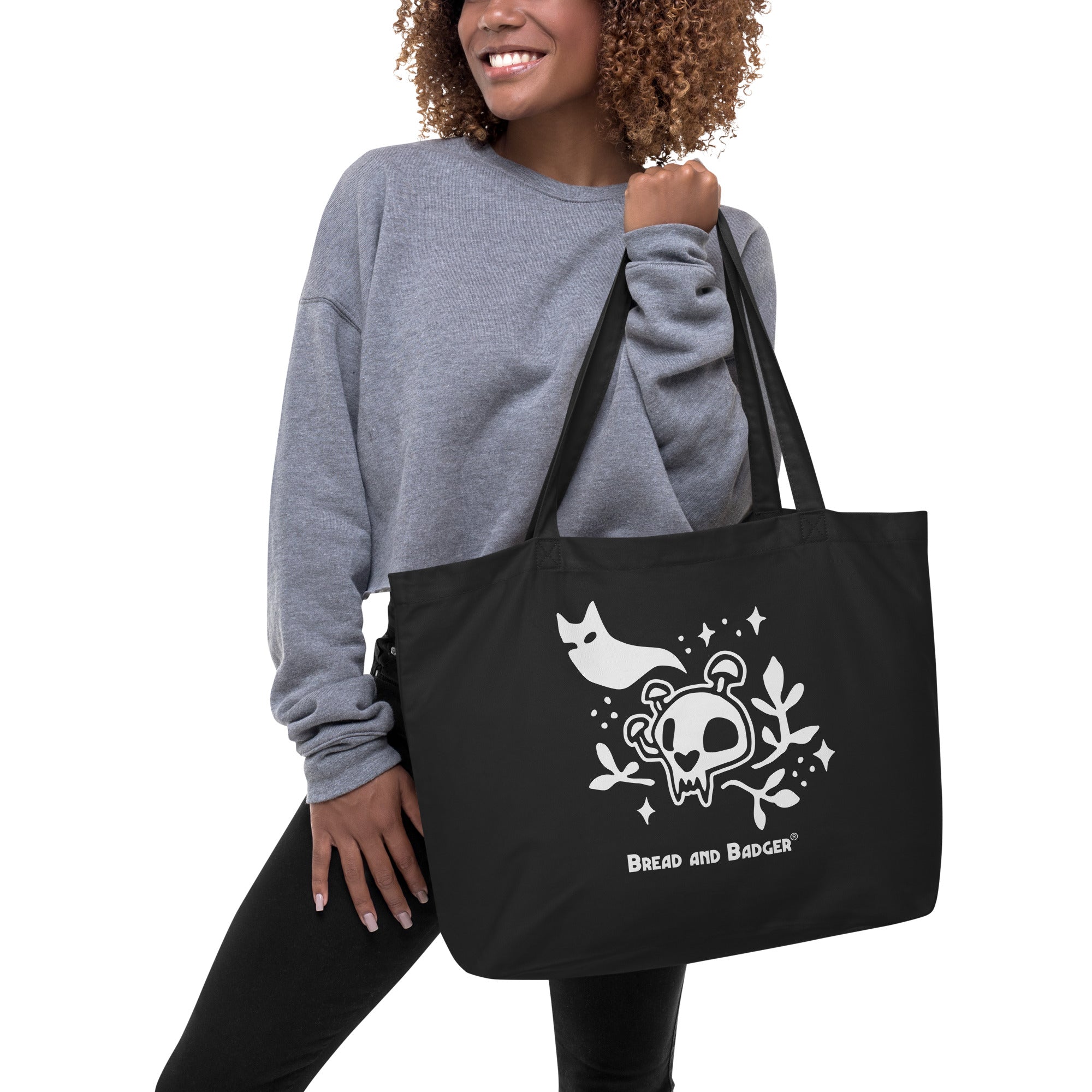 Person holding a black tote bag with white skull and cat ghost design and 'Bread and Badger' logo.