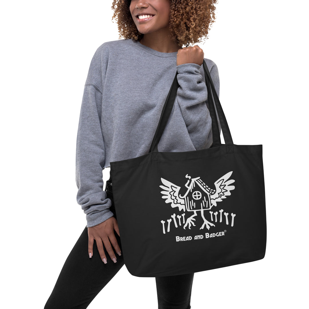 Person holding a black tote bag with a Baba Yaga's hut graphic and text on a white background