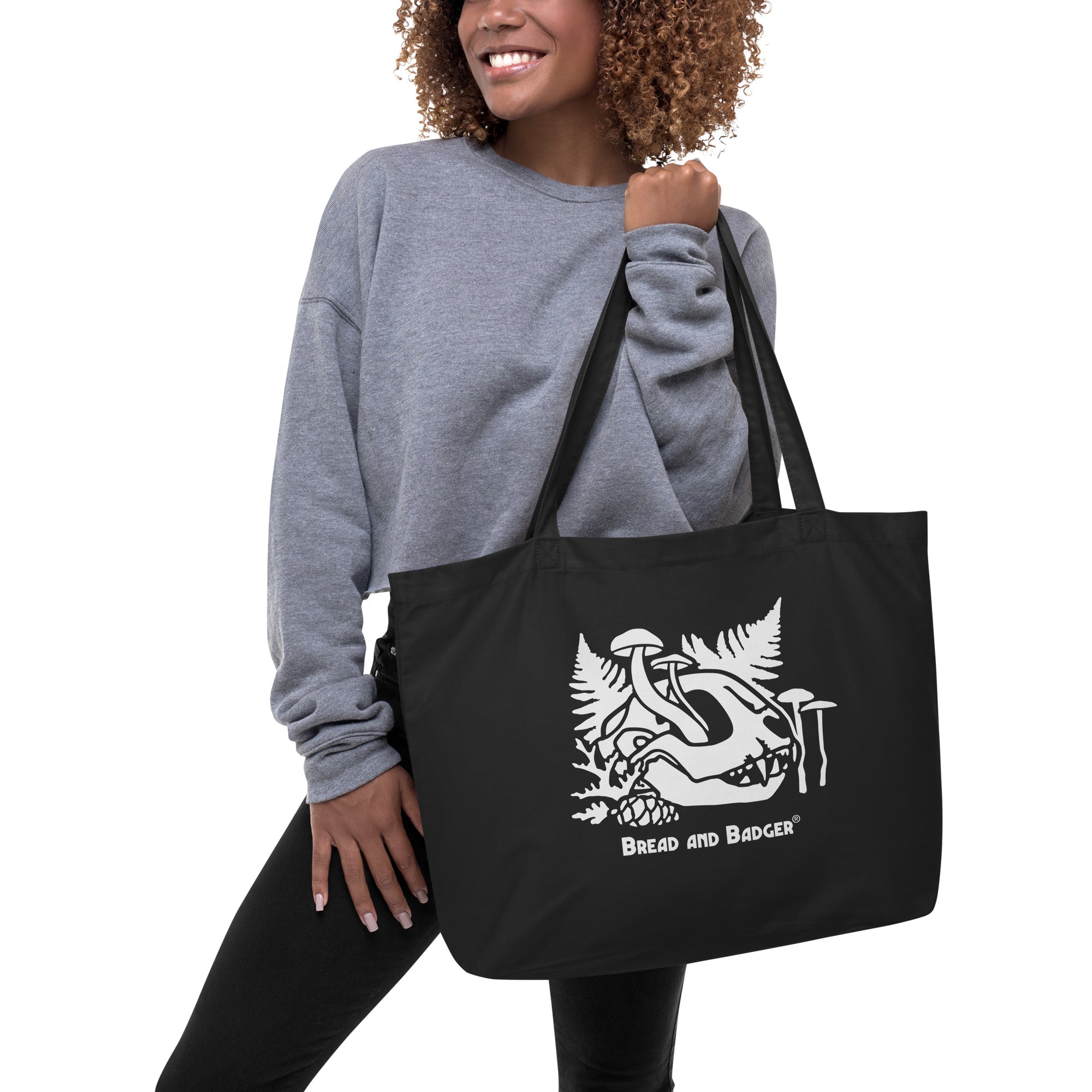 Woman holding a black tote bag with a white cat skull graphic and 'Bread and Badger' text on a white background