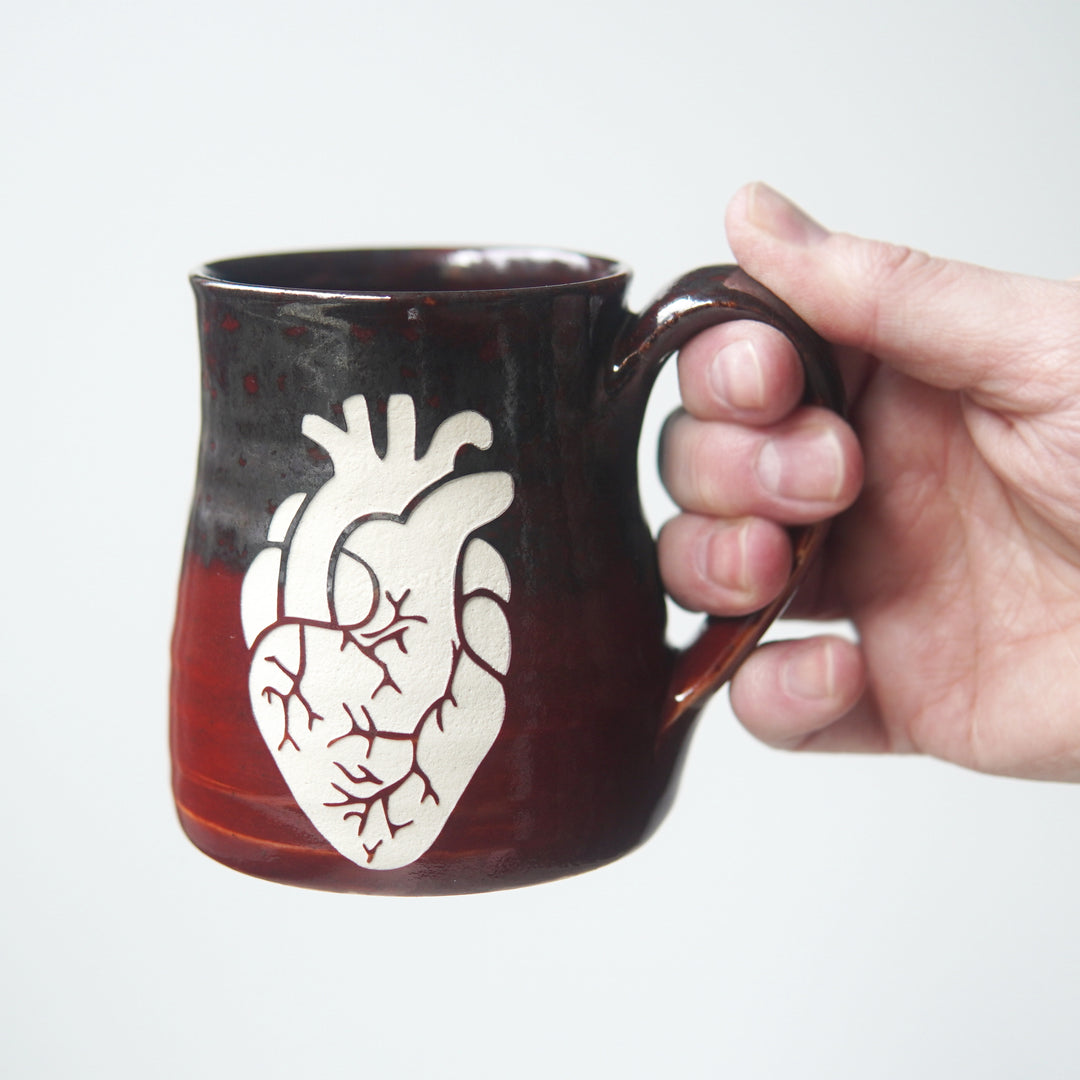 anatomical heart engraved on a red and silver mug, held by a hand