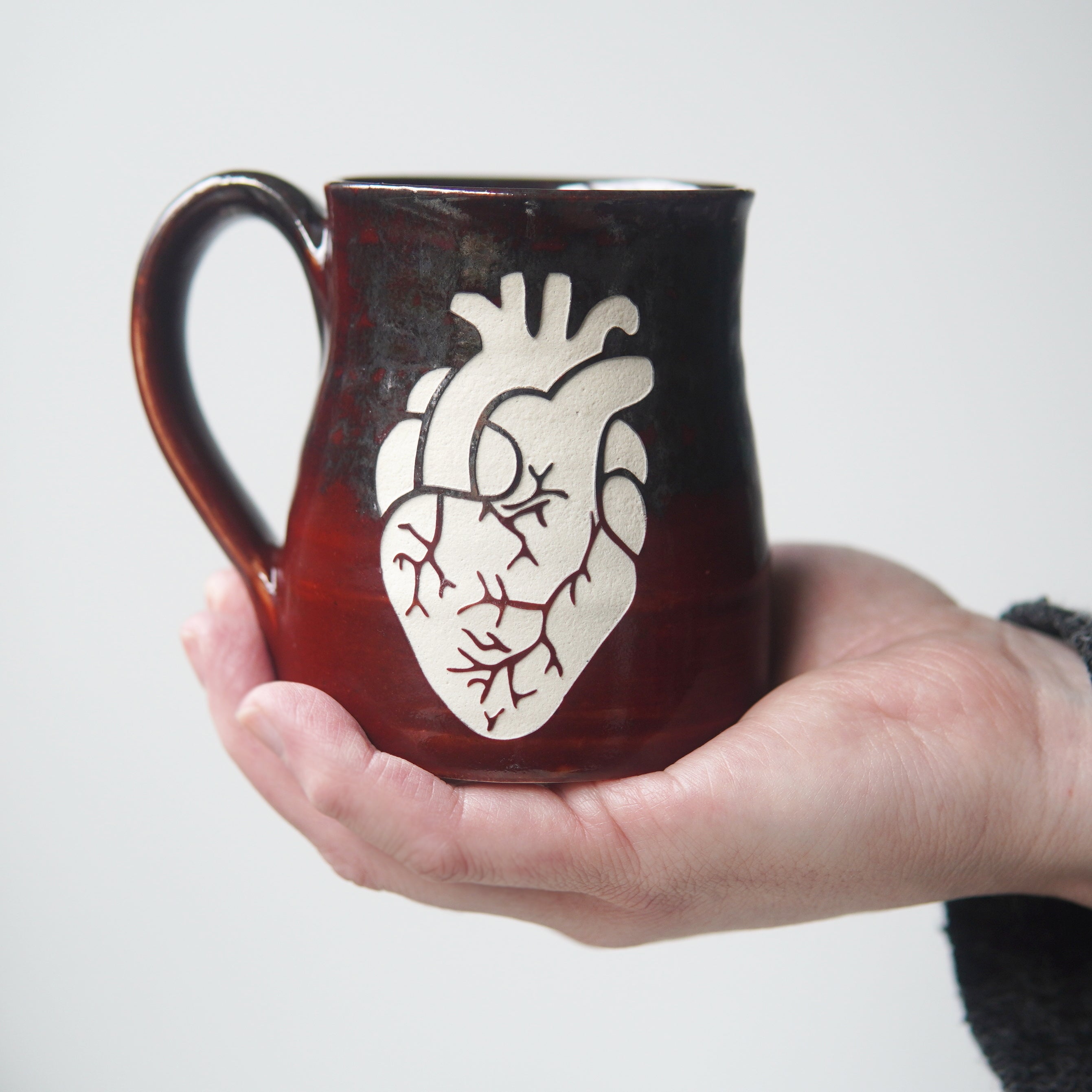 anatomical heart engraved on a red and silver mug, held by a hand