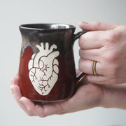 handmade pottery mug engraved with an anatomical heart, held in hands