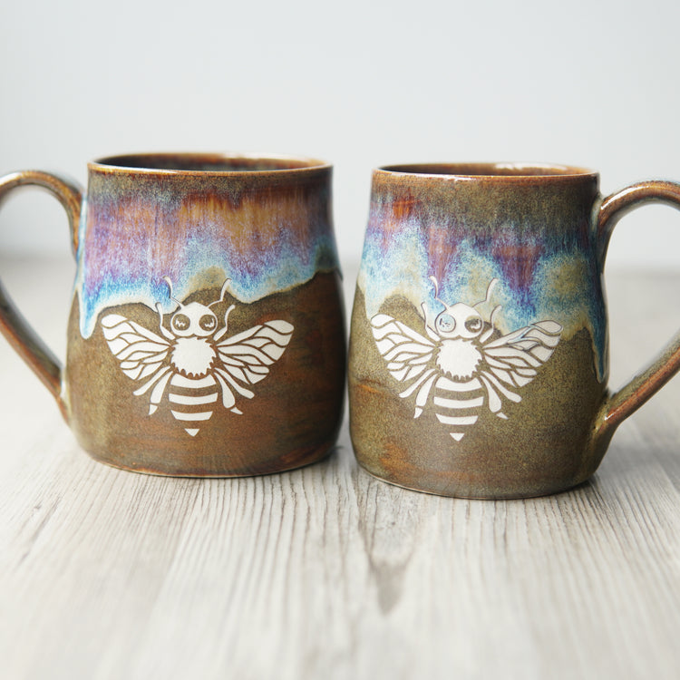 pair of pottery mugs engraved with a honey bee in "Dusk" colorway to show variations