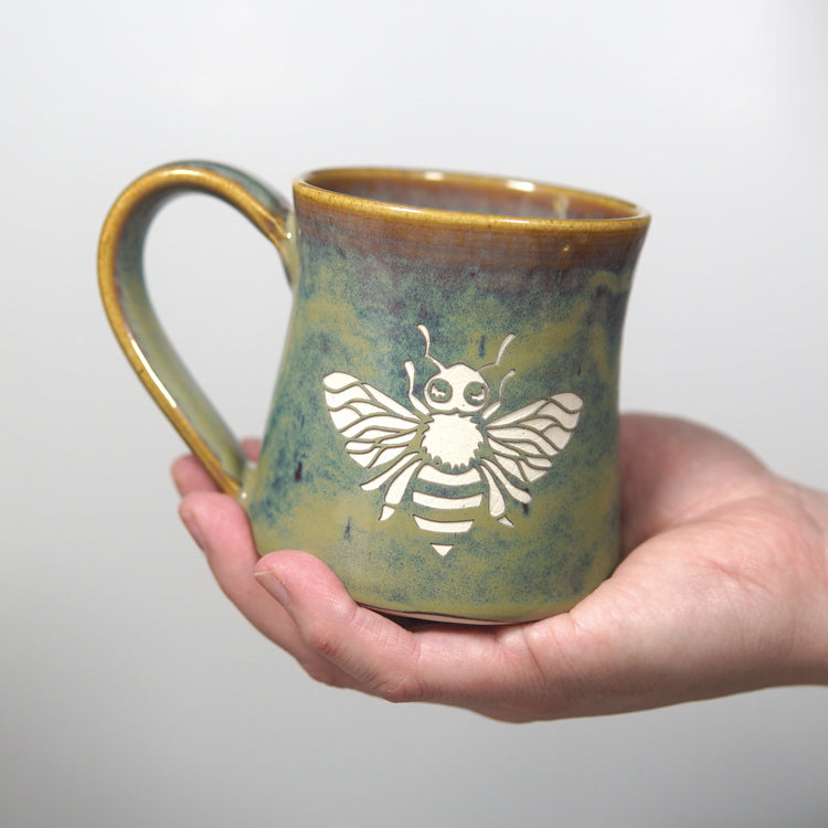 handmade mug engraved with a honey bee, held in a hand