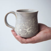 dogwood flower engraved onto a handmade mug, held in a hand
