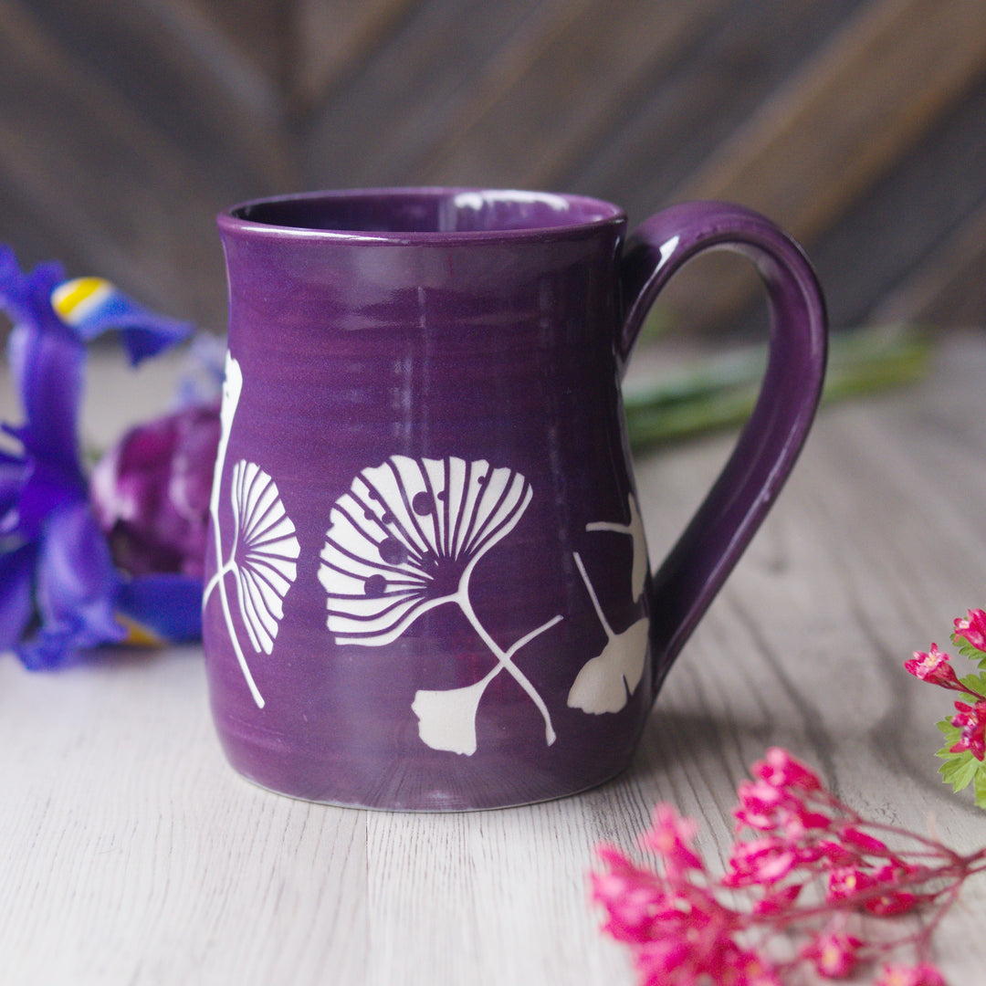 Purple mug with white floral design on a wooden surface with flowers