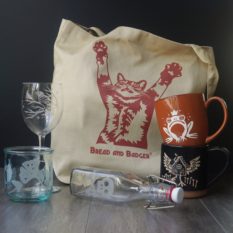 Tote bag with cat design, mugs, glasses, and a bottle on a dark background