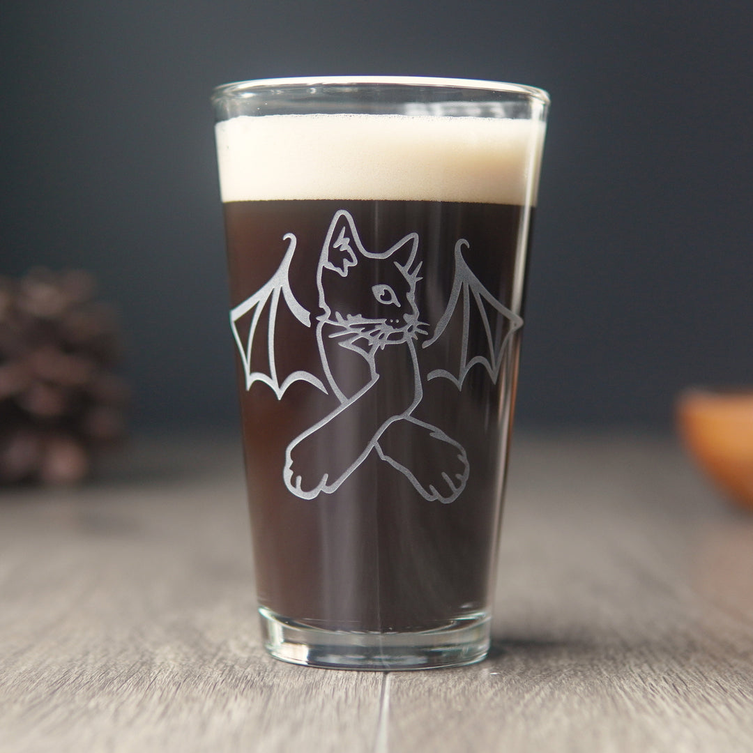 pint glass full of dark beer, engraved with a cat with bat wings