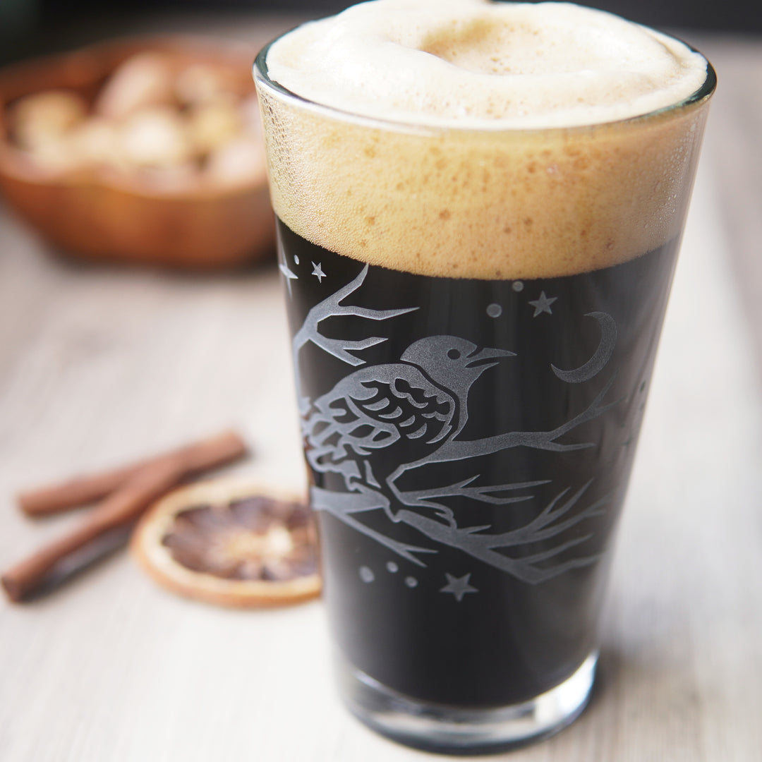 pint glass full of dark beer etched with a crow in a tree, stars, and a crescent moon