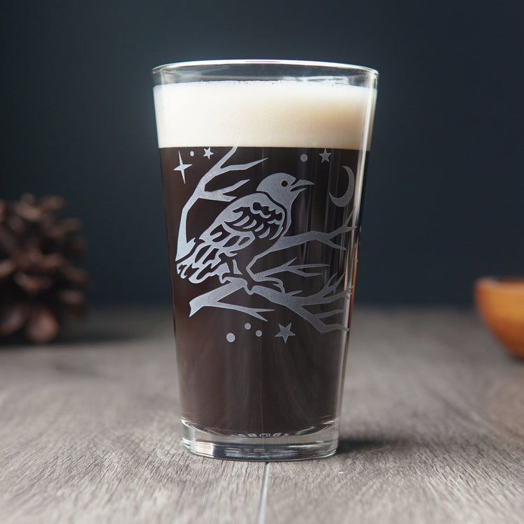 pint glass full of dark beer etched with a crow in a tree, stars, and a crescent moon