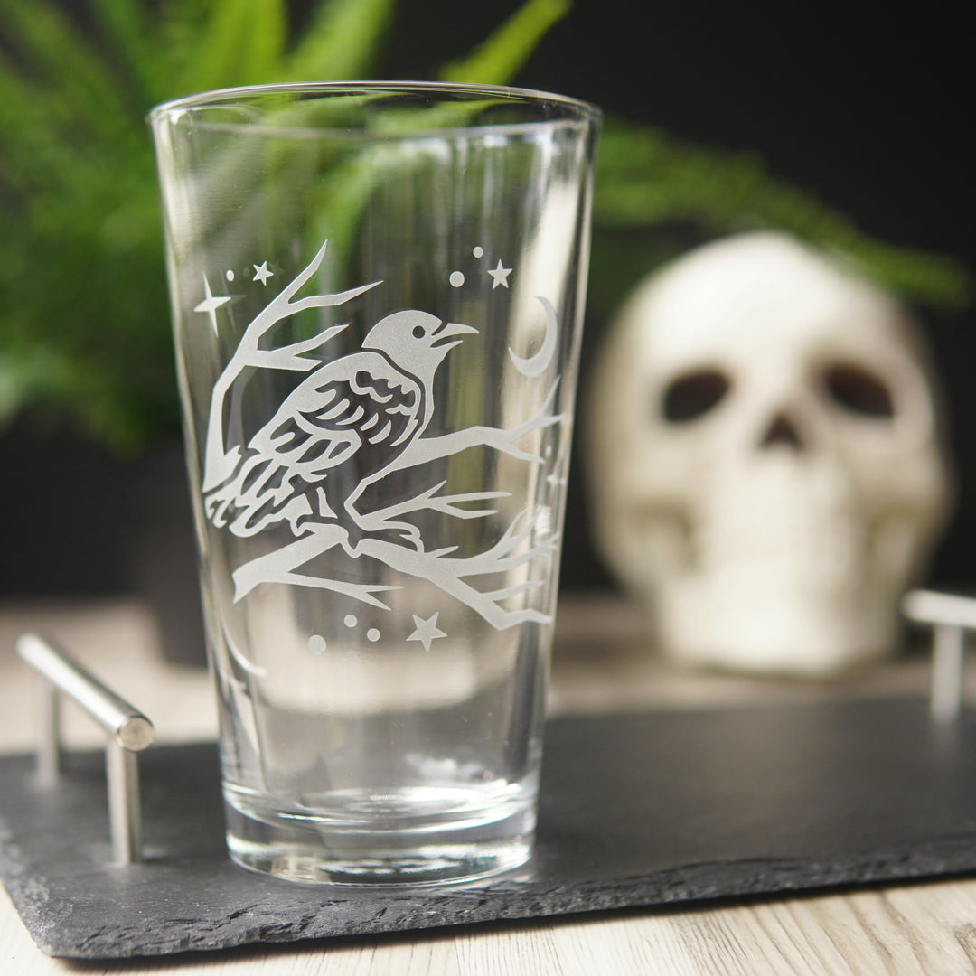 crow pint glass with a human skull and fern in the background