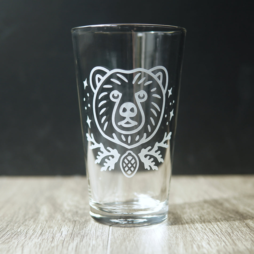 pint glass engraved with a bear's face, stars, cedar branches, and a pine cone