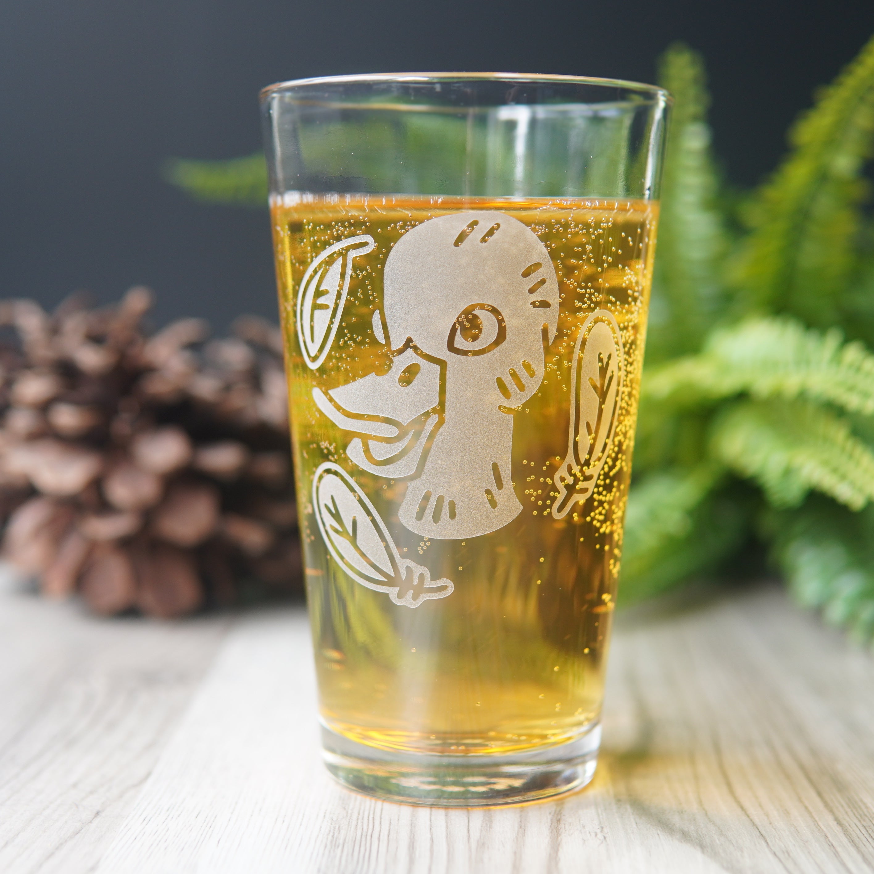 pint glass full of yellow beer engraved with a duck head, surrounded by three feathers