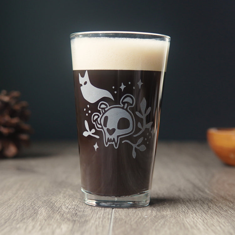 Pint glass full of dark beer engraved with a cartoonish cat skull with mushrooms growing on it. A cat ghost floats above, and sparkles and plants surround the skull.