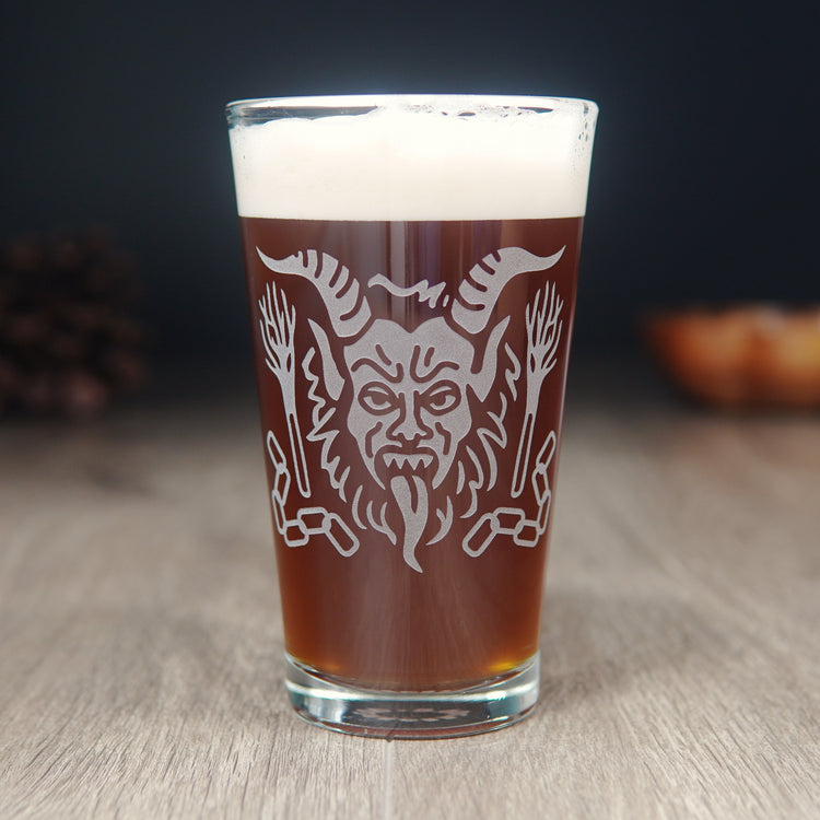 Pint glass engraved with Krampus' head and tongue hanging out. Chains and bundles of branches surround the head