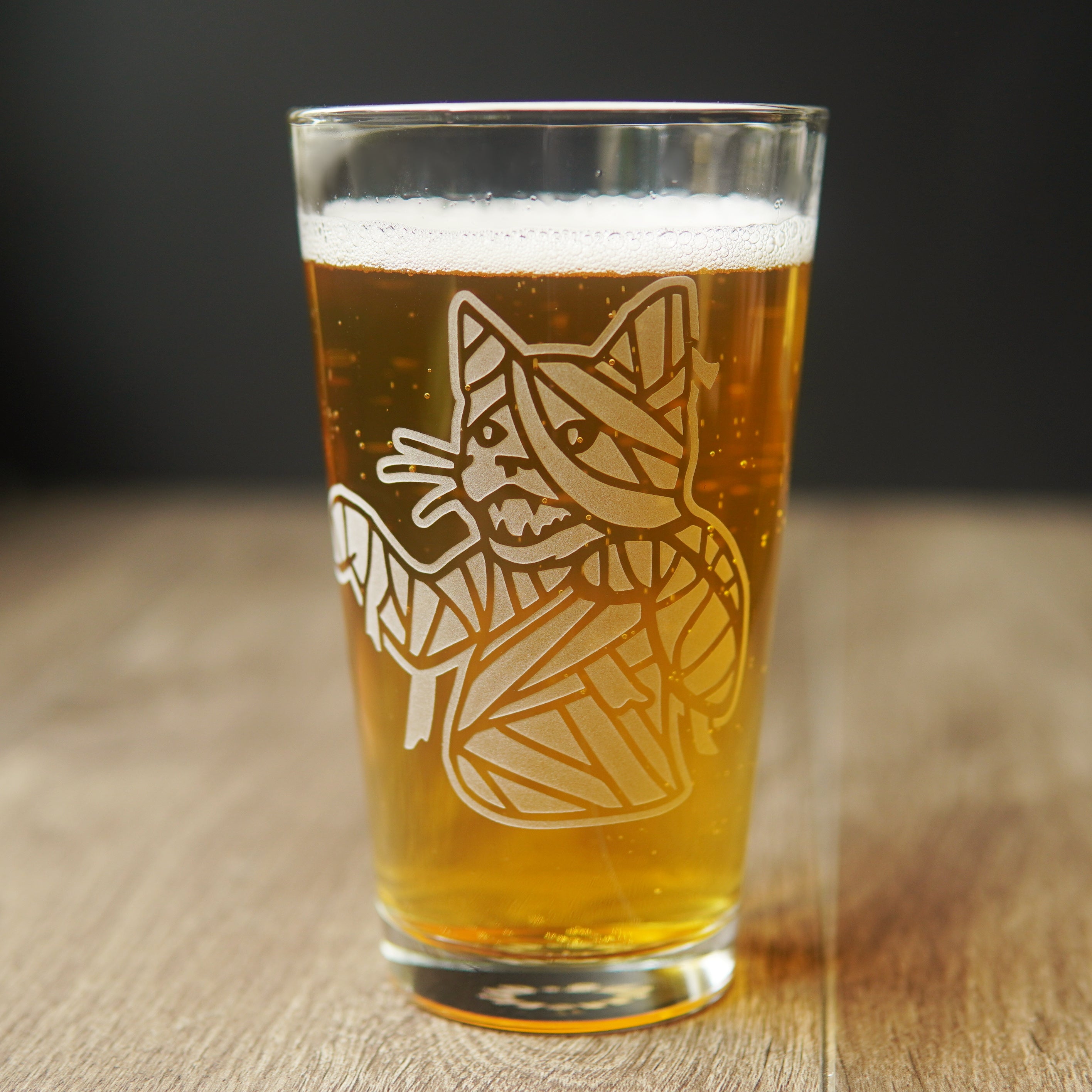 pint glass full of beer etched with the upper body of a mummy cat. The cat's mouth is open, arms slightly outstretched, and wrappings are coming loose.