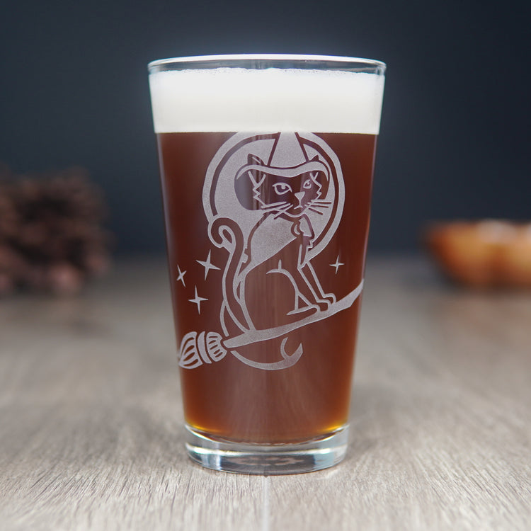 pint glass engraved with a witch cat on a flying broom in front of the full moon and stars