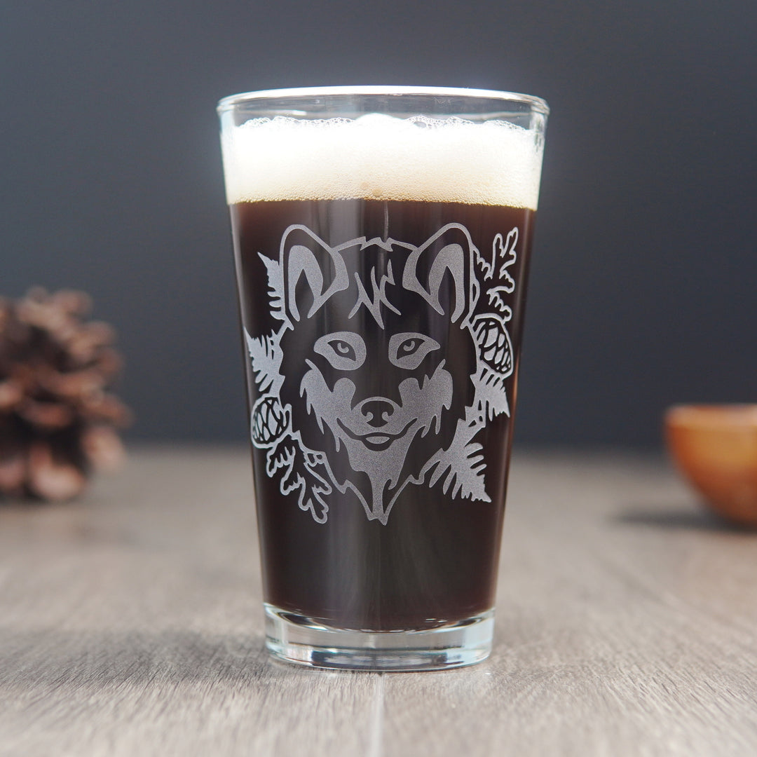 Pint glass engraved with a wolf's face, ferns, cedar branches, and pine cones