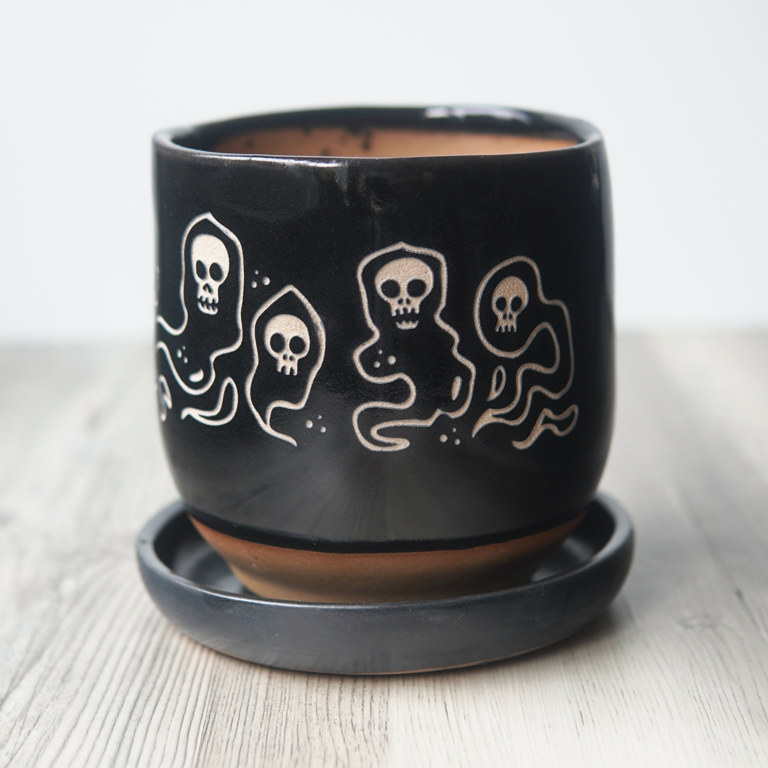 Black pot with white ghost designs on a light wooden surface