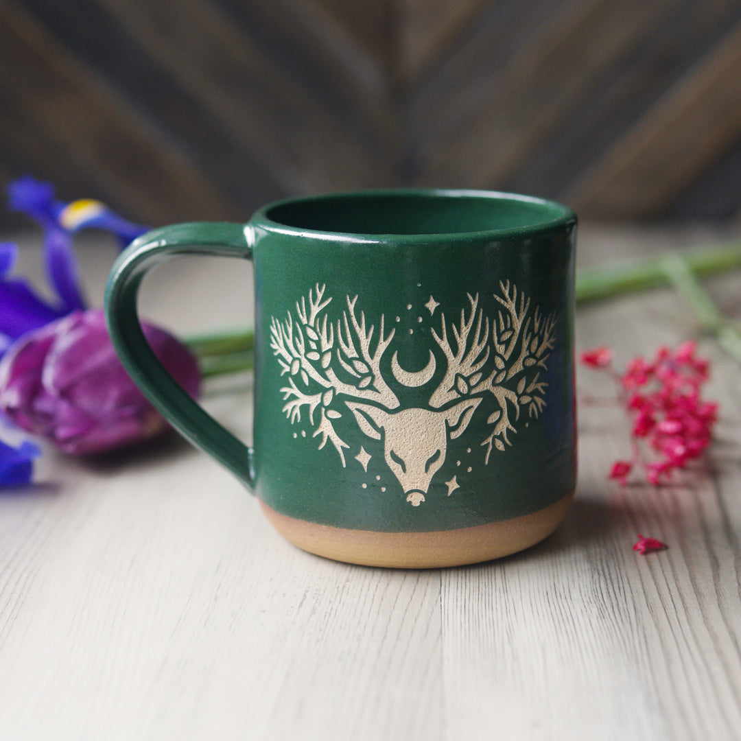 Green mug with deer design on a wooden surface with flowers in the background