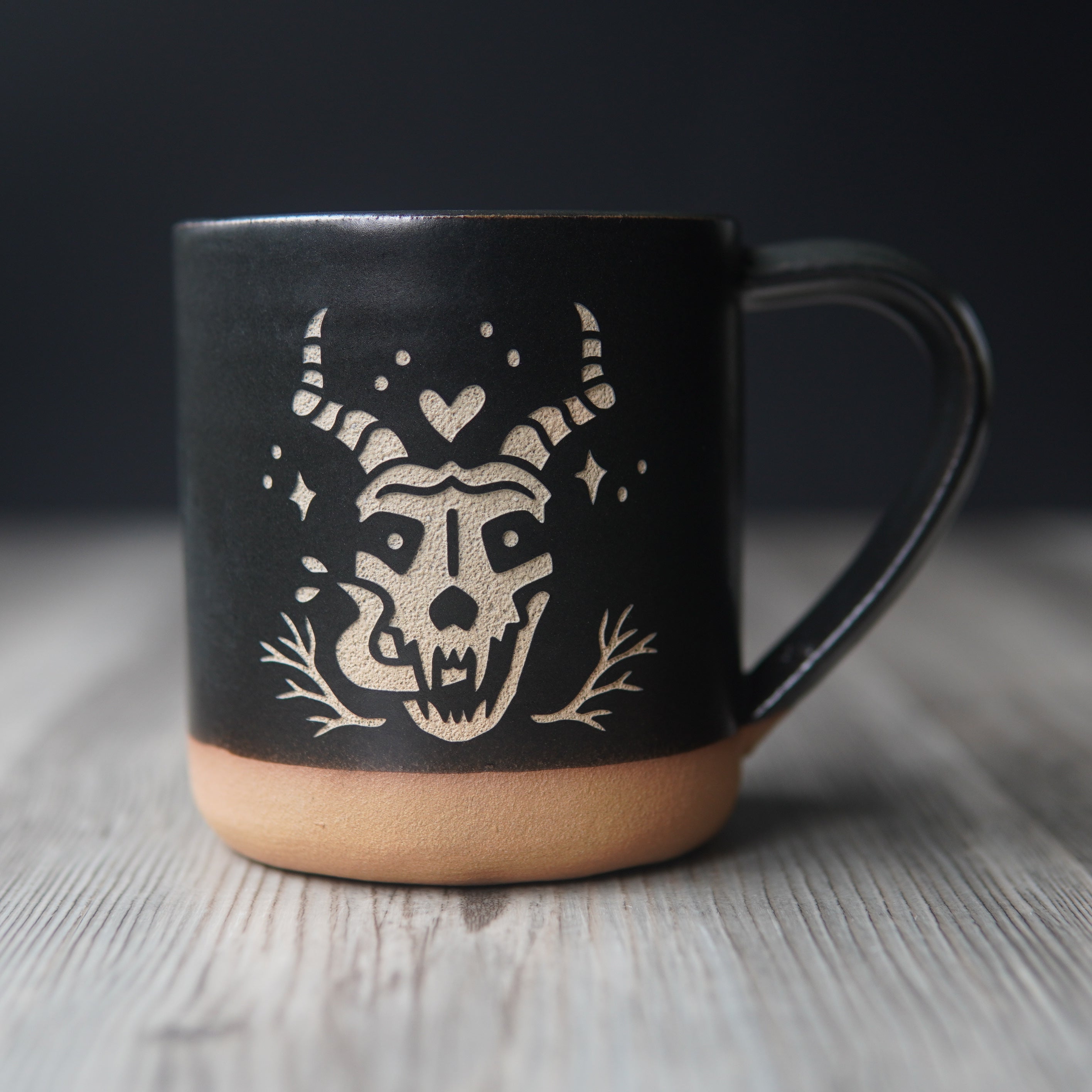skull with horns and long tongue engraved on a black mug