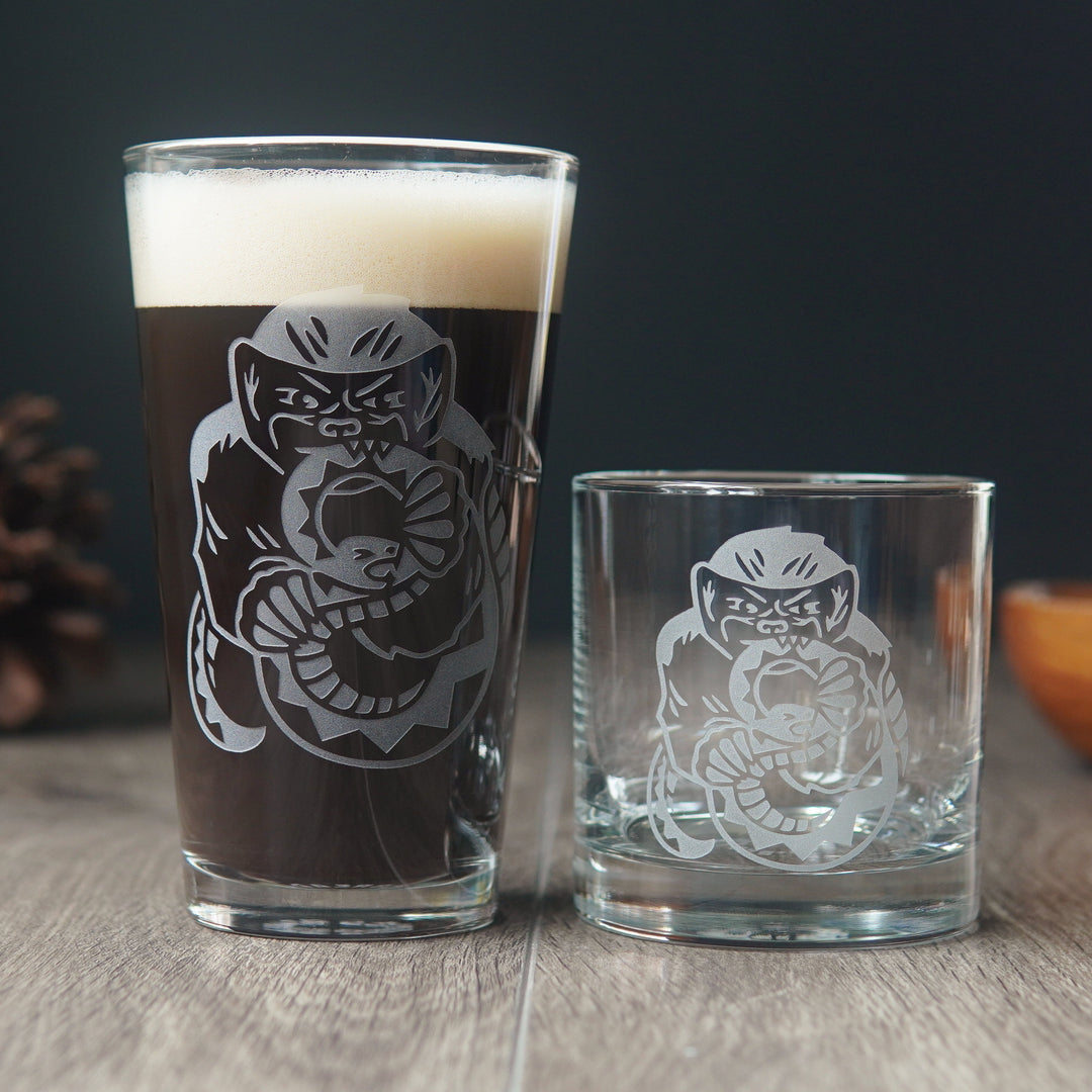 Pint glass and lowball glass, both etched with honey badgers. The badger is gnawing on a large snake, which is grimacing