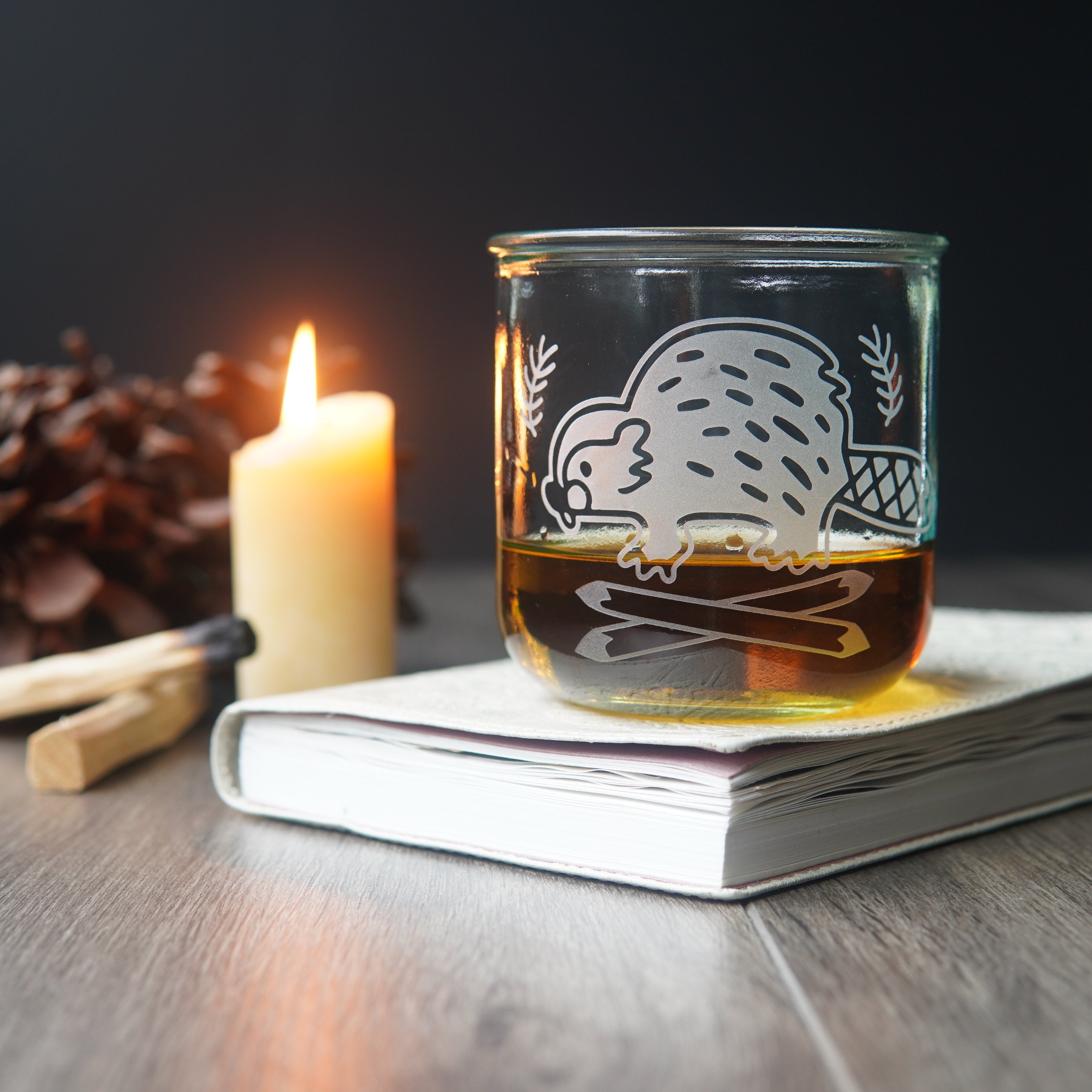 short recycled glass cup engraved with a cute beaver, with a portion of dark amber liquid inside it.