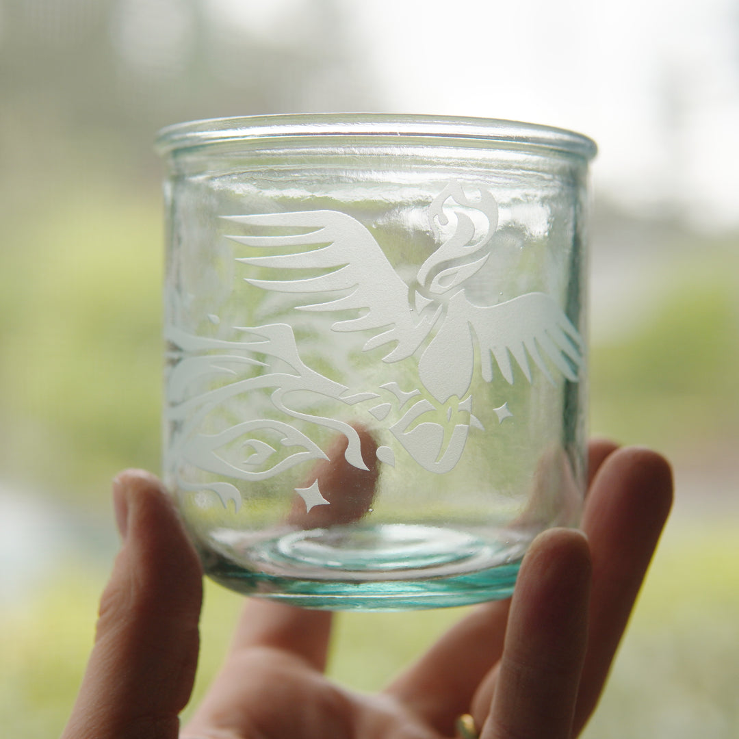 Phoenix bird engraved onto short glass, held by a hand