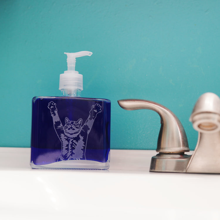 cat soap dispenser; square pump bottle next to a bathroom faucet and bright blue wall