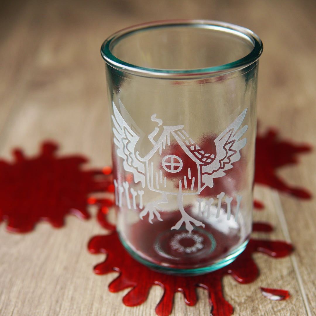 Baba Yaga's Hut etched onto a tall recycled glass cup, sitting on a table with fake blood splatters