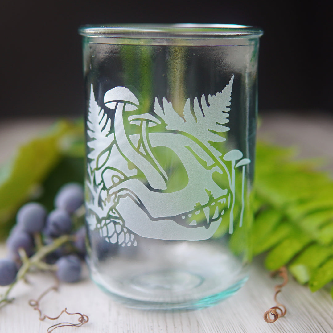 decaying cat skull with mushrooms and ferns etched onto a tall glass