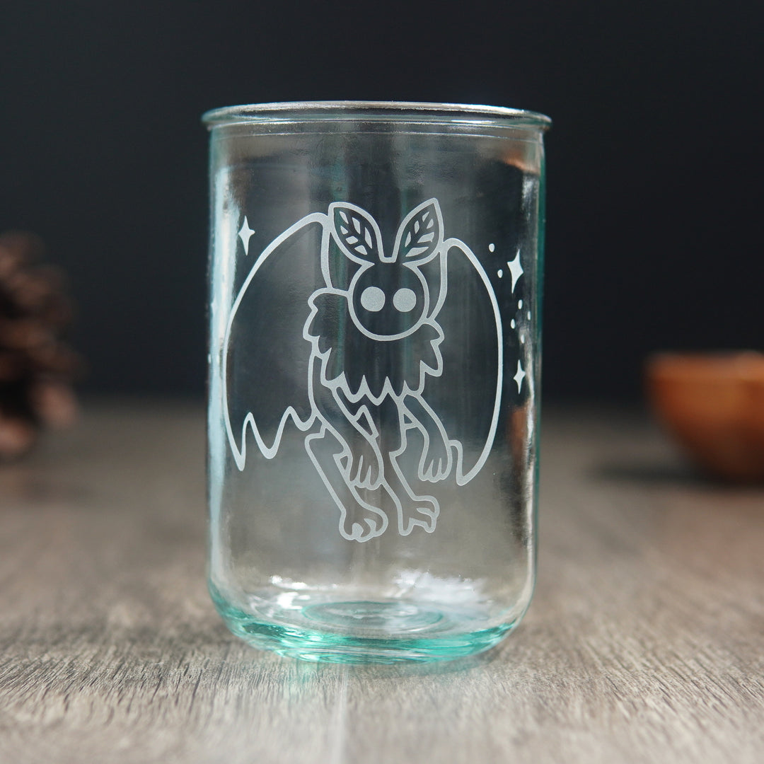 cute mothman surrounded by stars engraved onto a bluegreen-tinged tall glass