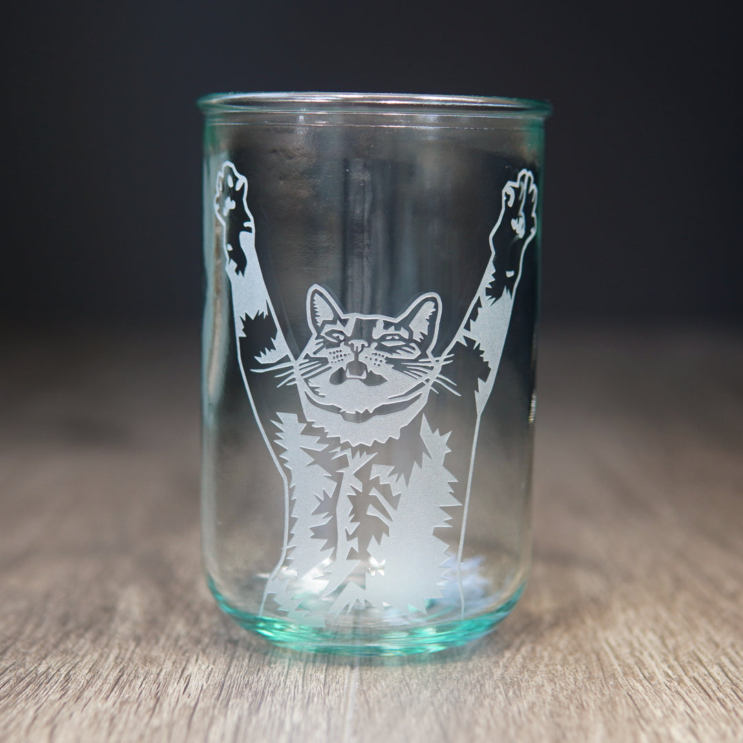 top half of a tabby cat with its arms stretched up and mouth slightly open engraved onto a tall glass