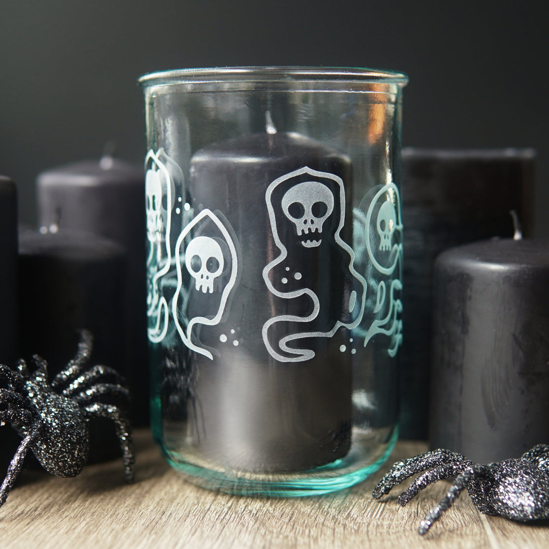 floating skull ghosts etched around a tall glass with black candles and plastic spiders