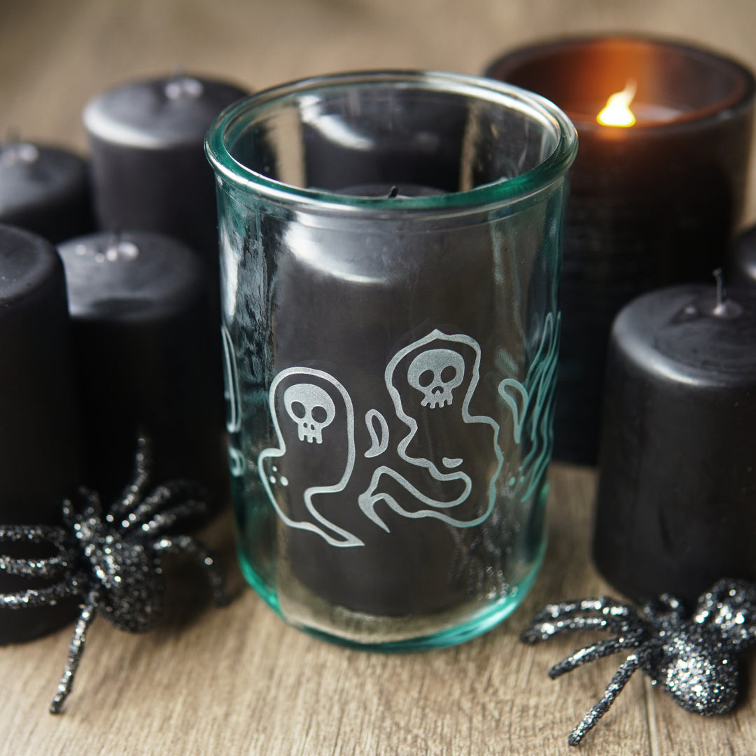 floating skull ghosts etched around a tall glass with black pillar candles