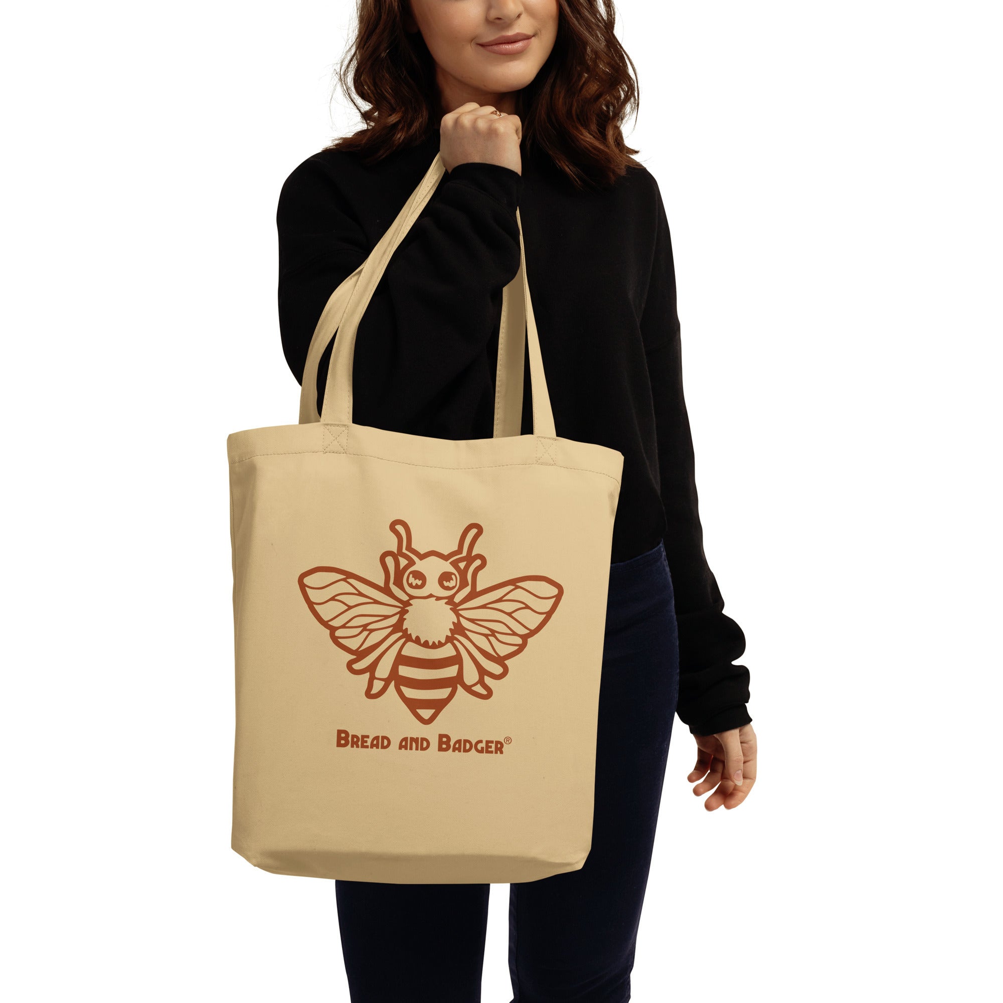 Person holding a beige tote bag with a bee design and 'Bread and Badger' text on a white background