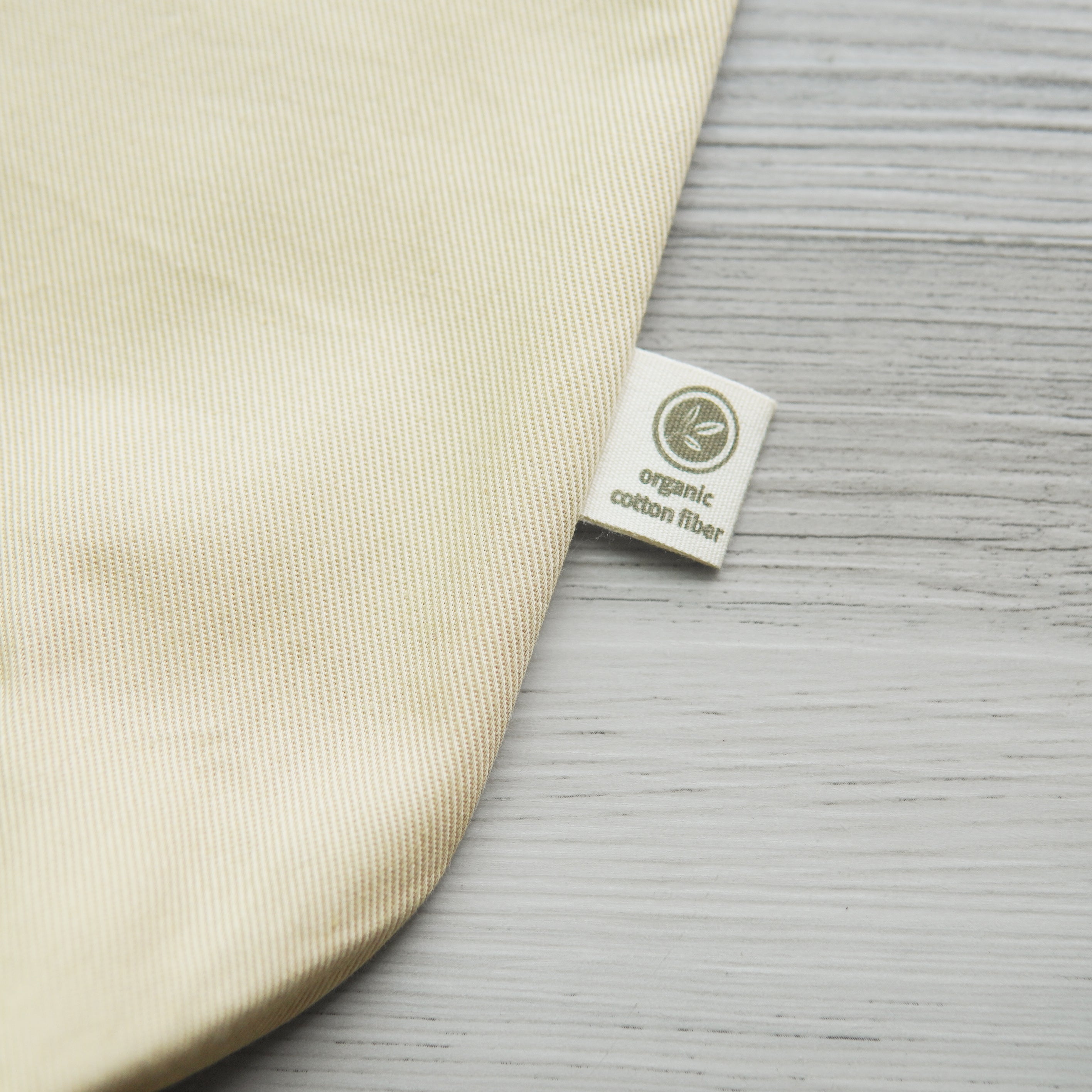small tag printed with a leaf design and the text, "organic cotton fiber" on the outside edge of a beige tote bag
