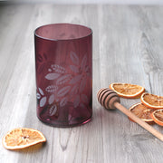 Tea Leaves engraved onto blown glass tumbler in translucent black cherry red next to orange slices and a wooden honey dipper