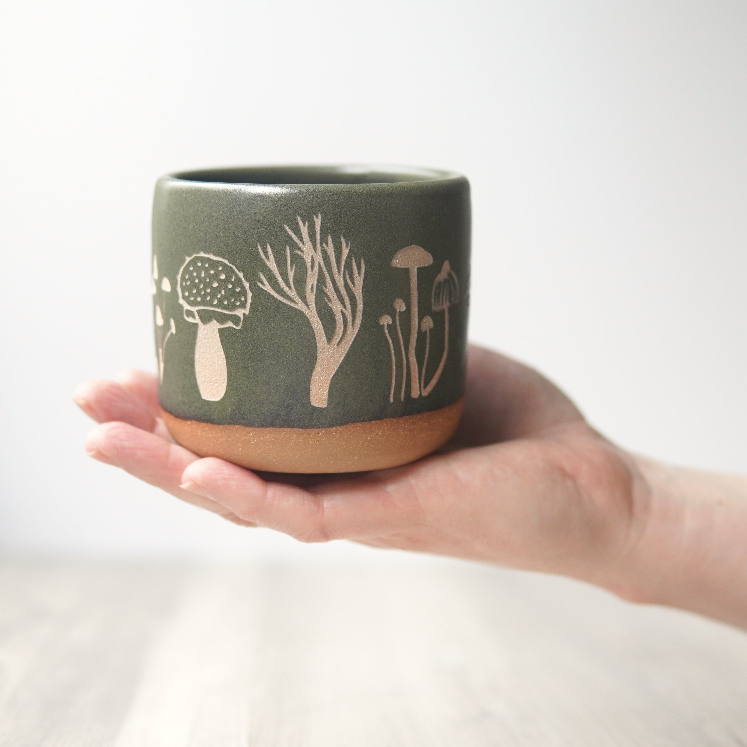 Mushroom mug in moss green, resting on an open hand