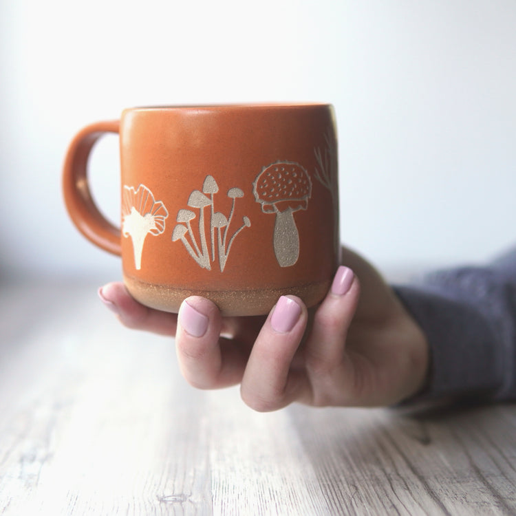 Mushrooms Forest Style Mug in Pumpkin Orange, held in a hand