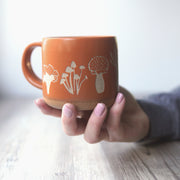 Mushrooms Forest Style Mug in Pumpkin Orange, held in a hand