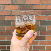 Bald eagle etched lowball cocktail glass by Bread and Badger, held in front of a brick wall