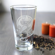 Witch Cat on a broom etched onto a pint glass next to fall votive candles and loose-leaf chai tea