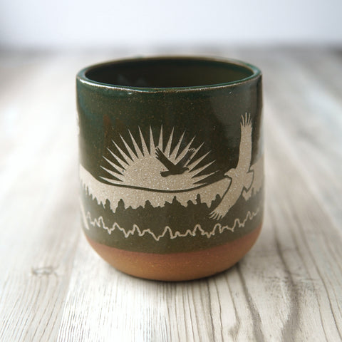 Bald Eagles engraved handmade pottery mug in pine green, with eagles soaring in front of a setting sun, mountains, and pine trees